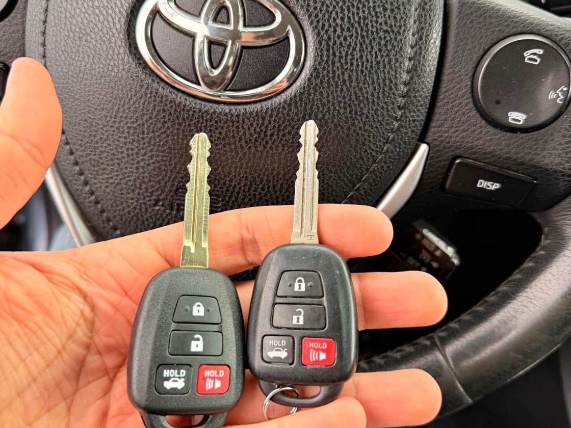 Two Toyota remote head keys held in front of a Toyota steering wheel